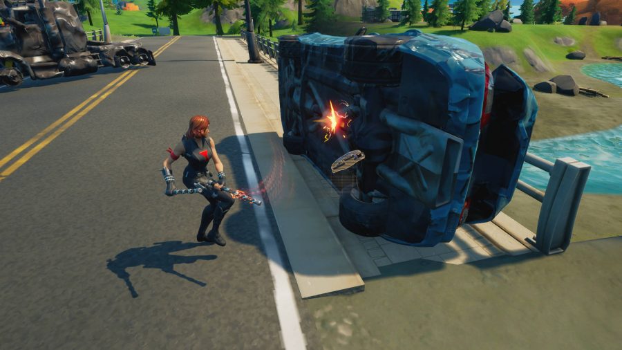 Der Spieler hackt an einem umgedrehten Auto herum, um mechanische Teile für die Herstellung in Fortnite zu ernten. An explodierter Lastwagen ist in der Nähe.