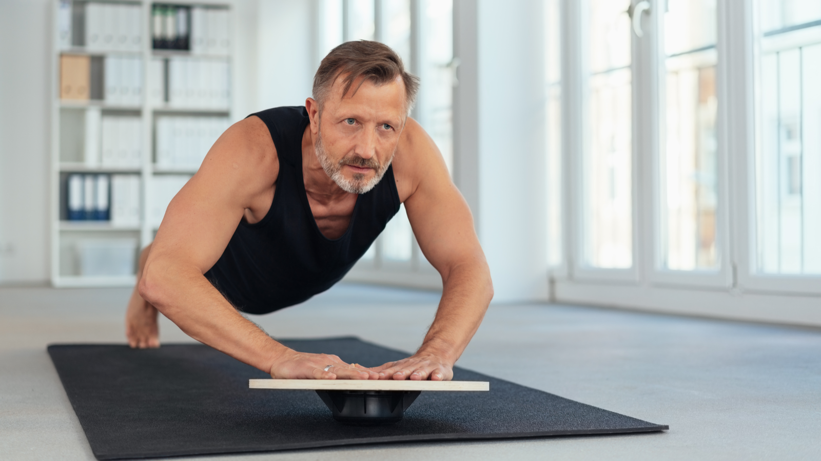 Personne d'âge moyen en forme exerçant une variation de planche avec les mains sur une planche d'équilibre à l'intérieur