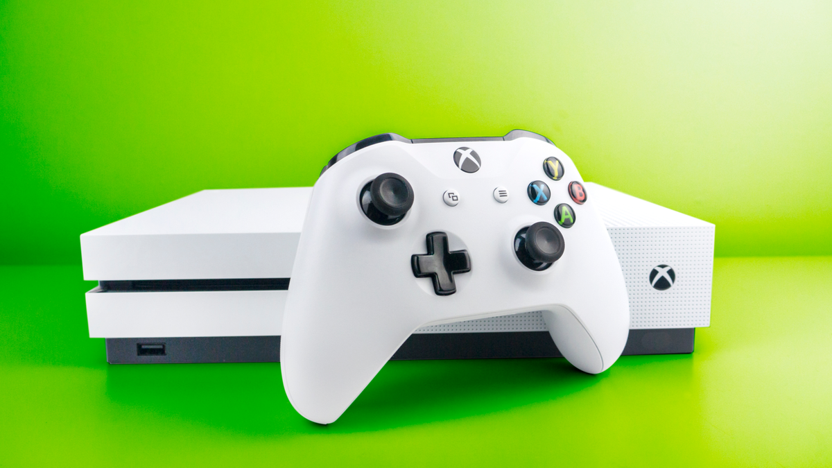 Console Xbox One S blanche et manette assortie devant un fond vert gradué dynamiquement