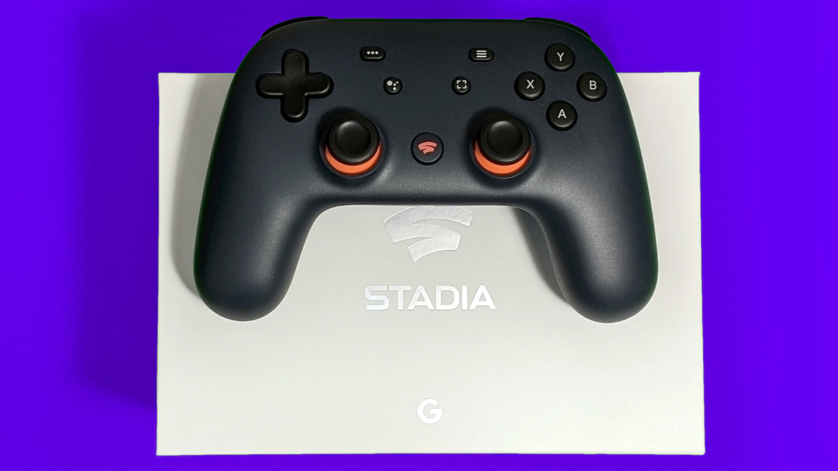 Closeup pengontrol Google Stadia yang diletakkan di atas kotak Stadia putih dengan latar belakang ungu cerah