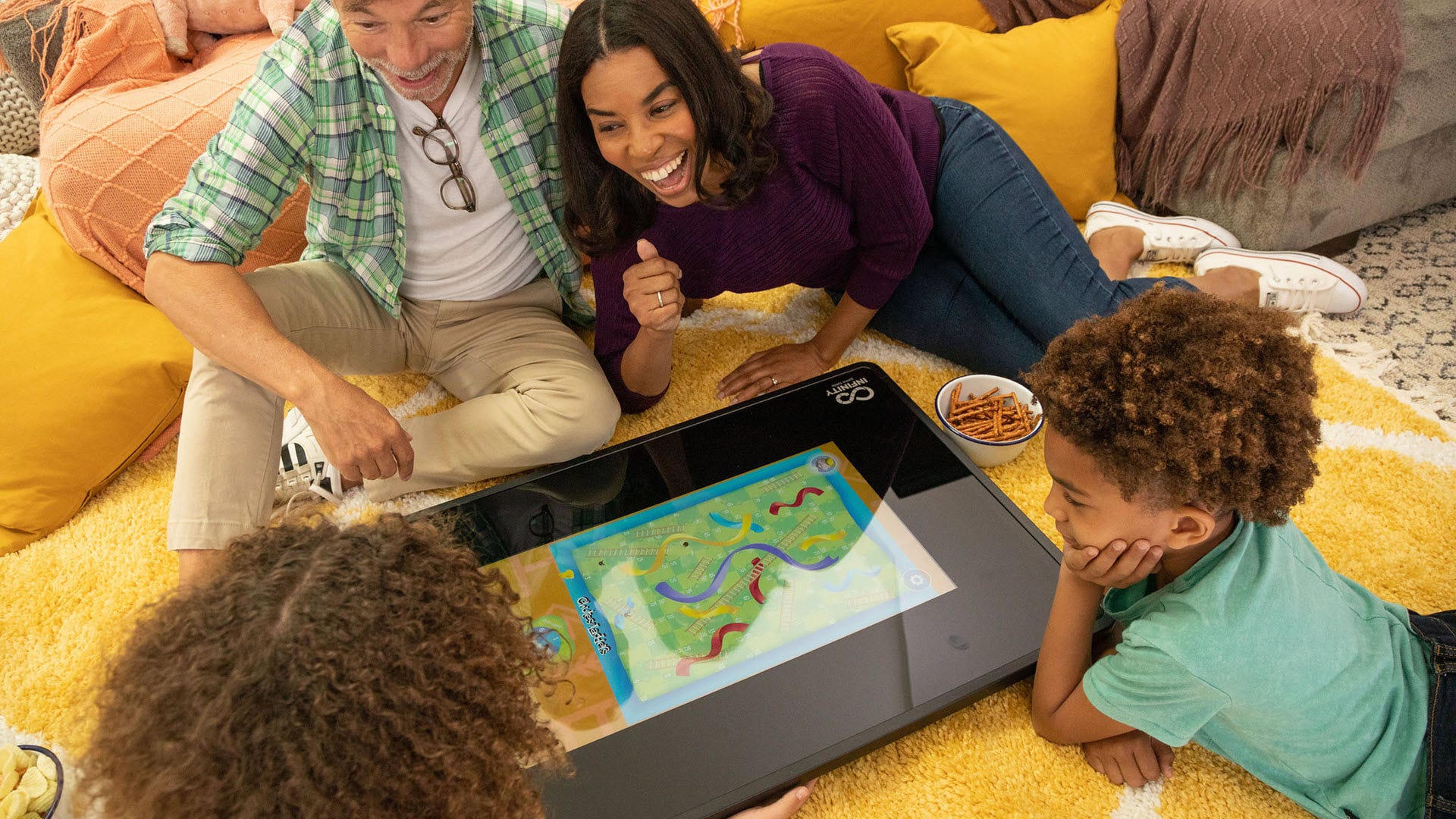 Quattro persone che giocano a'Scivoli e scale'sul pavimento con un tavolo da gioco digitale.