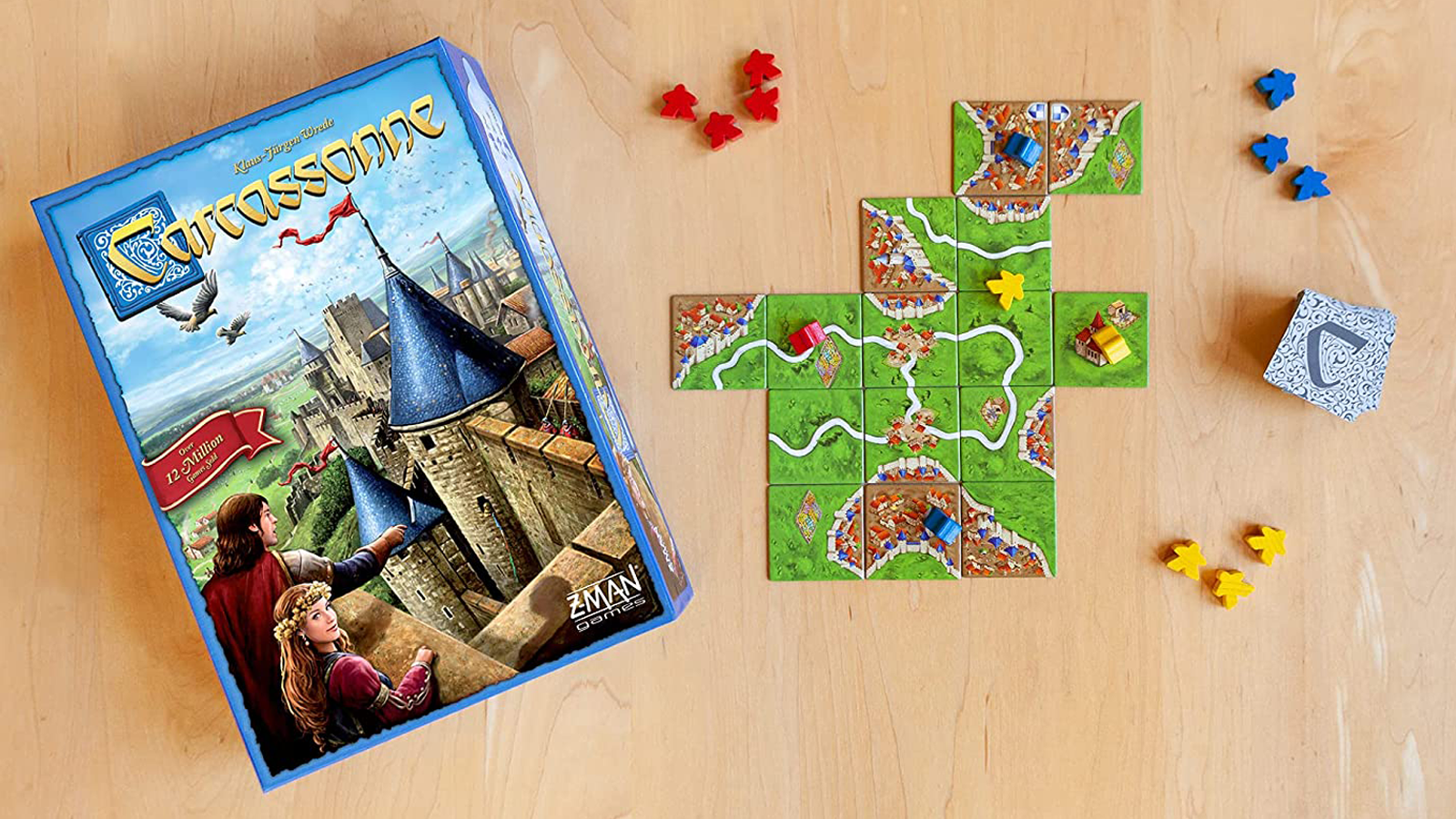 Scatola gioco da tavolo Carcassonne su tavolo di legno accanto a tessere e meeples