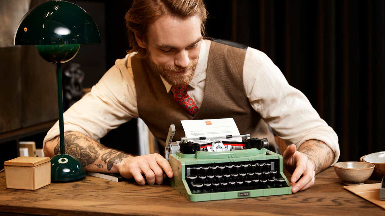 Persona vestita con abiti d'altri tempi seduta alla scrivania di legno con LEGO Typewriter e altre decorazioni