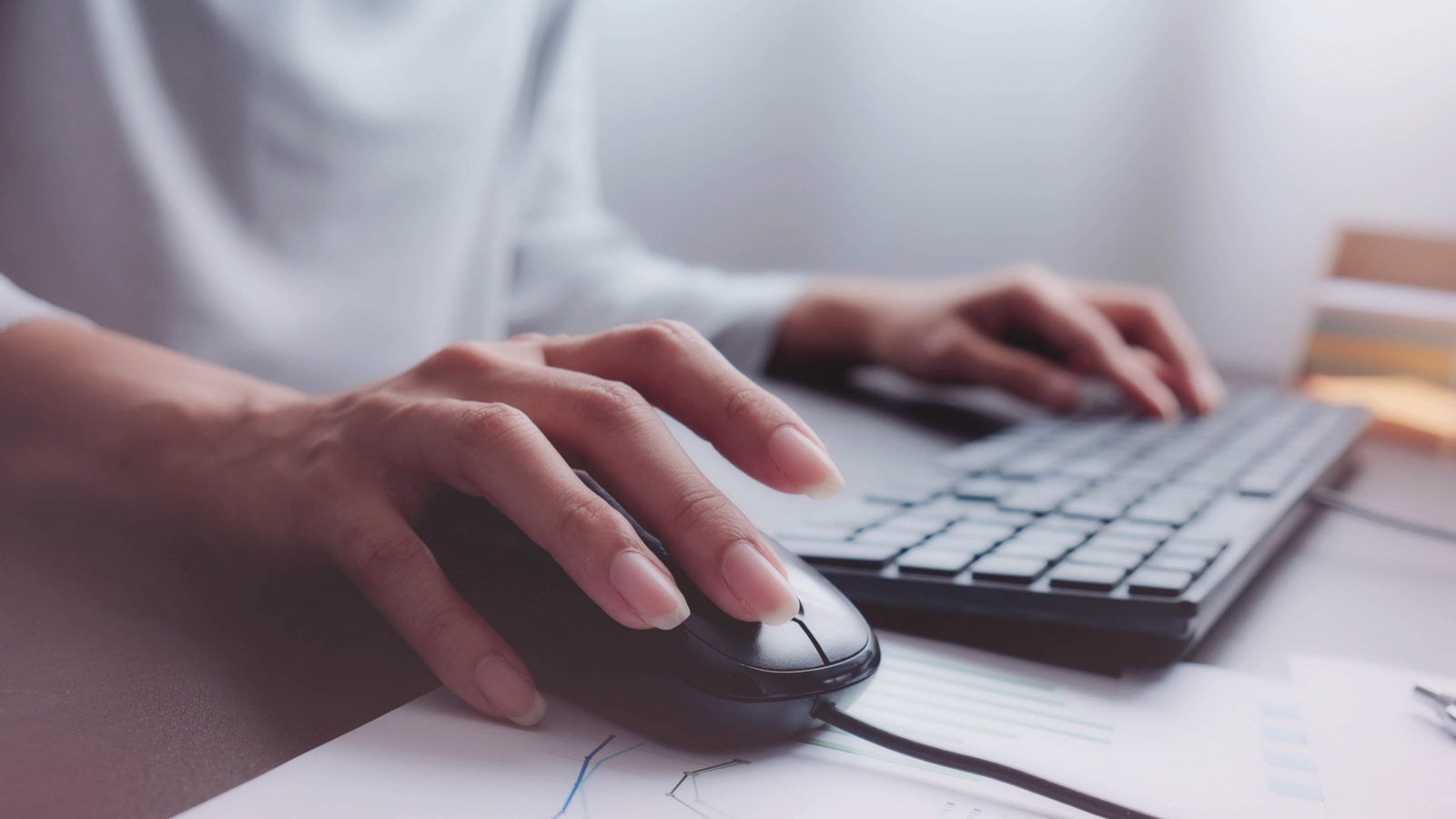 Persoon die een computertoetsenbord en muis gebruikt aan een bureau