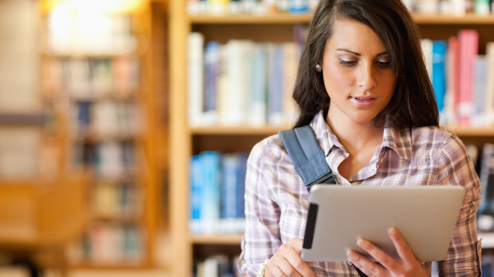 Jonge gefocuste student die een tablet gebruikt in een universiteitsbibliotheek