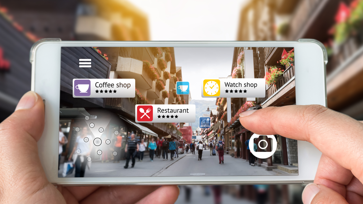 มือของบุคคลกำลังถือสมาร์ทโฟนโดยใช้แอป Augmented Reality เพื่อตรวจสอบข้อมูลเกี่ยวกับธุรกิจใกล้เคียงขณะเดินไปตามถนน