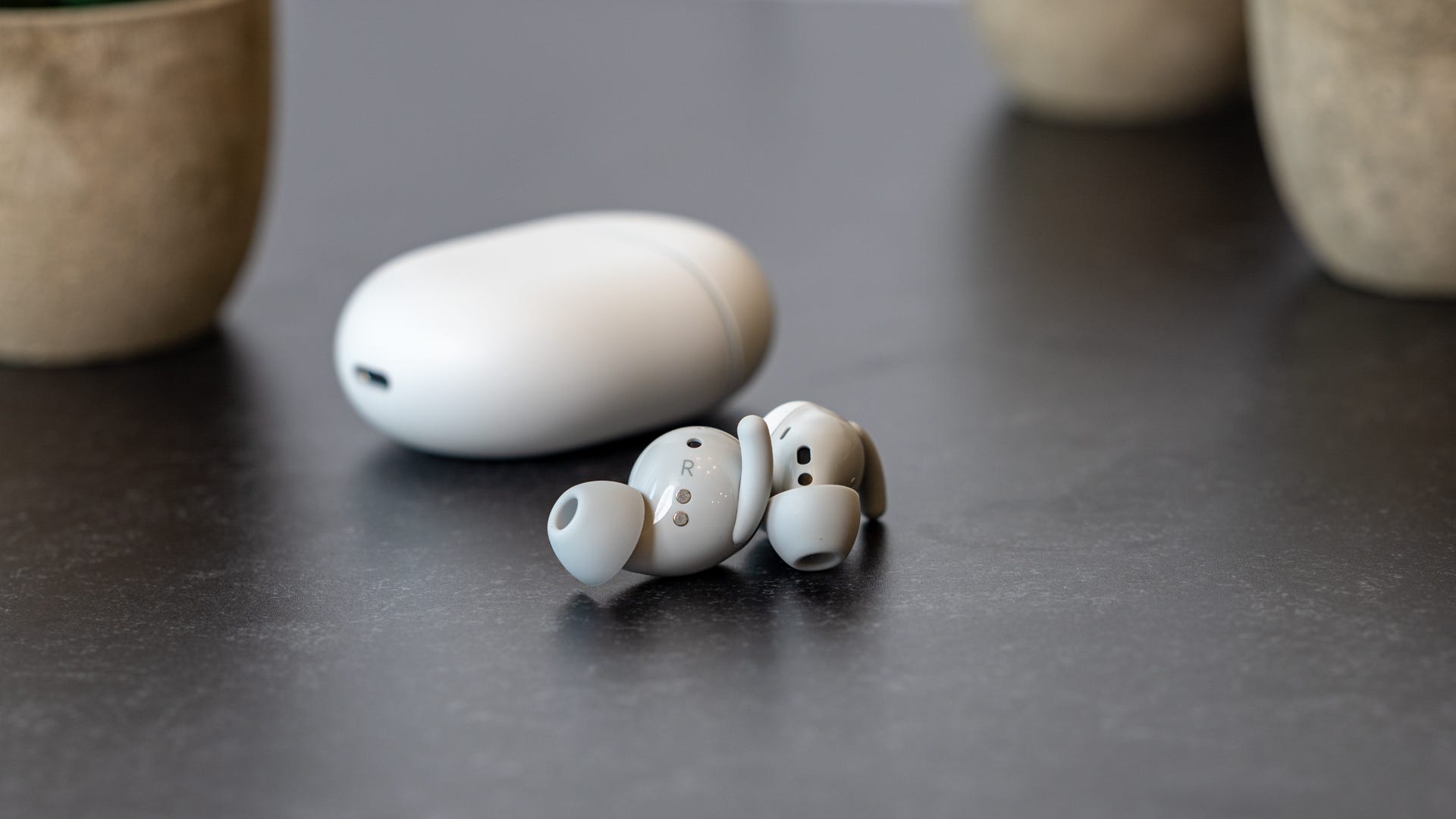 Pixel Buds A Series บนโต๊ะโดยมีเคสอยู่ด้านหลัง