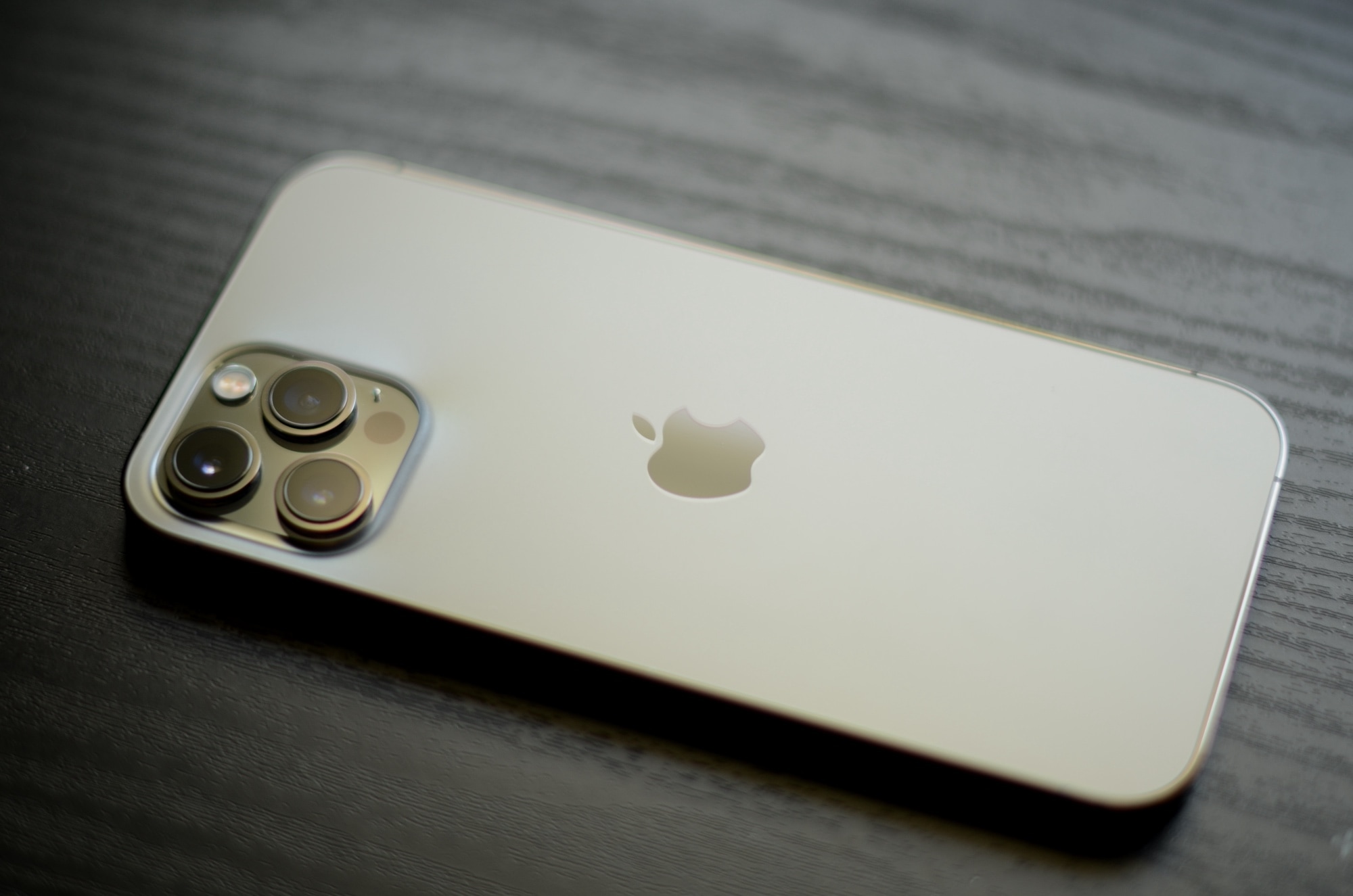 Một chiếc iPhone 12 Pro Max màu vàng được đặt úp xuống bàn gỗ