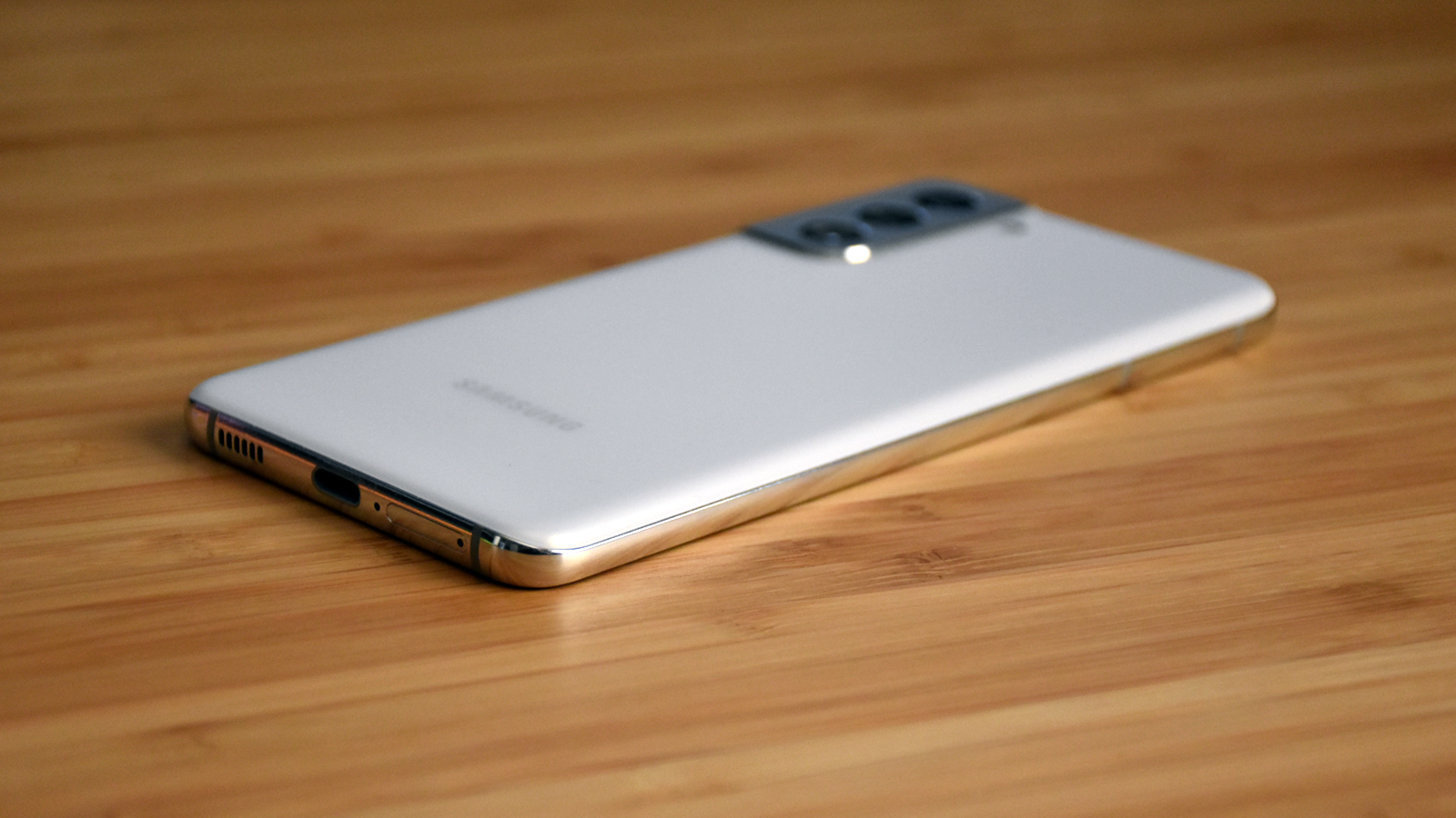 Góc nhìn từ phía sau và phía dưới của Samsung Galaxy S21 trên bàn gỗ
