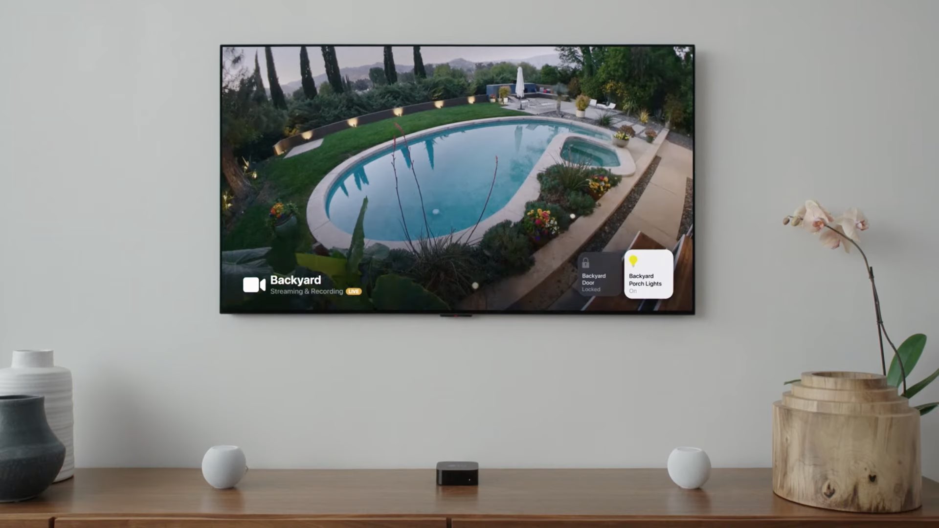Uma imagem que mostra o feed de uma câmera de segurança HomeKit exibida na Apple TV com tvOS 15, com controles de iluminação inteligentes visíveis nos cantos da tela