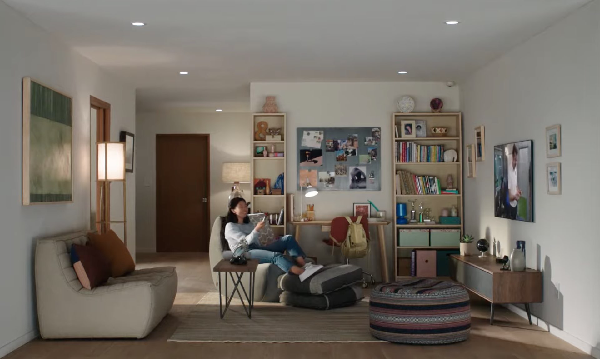 Uma imagem de estilo de vida mostrando uma casa com uma jovem sentada no sofá, sorrindo e assistindo Apple TV e segurando o Siri Remote na mão direita